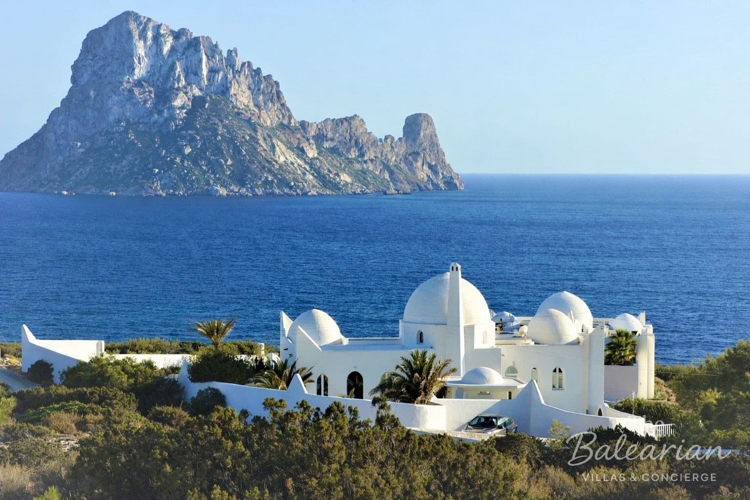 White villa with domes on the coast of Ibiza, with Es Vedrà in the background