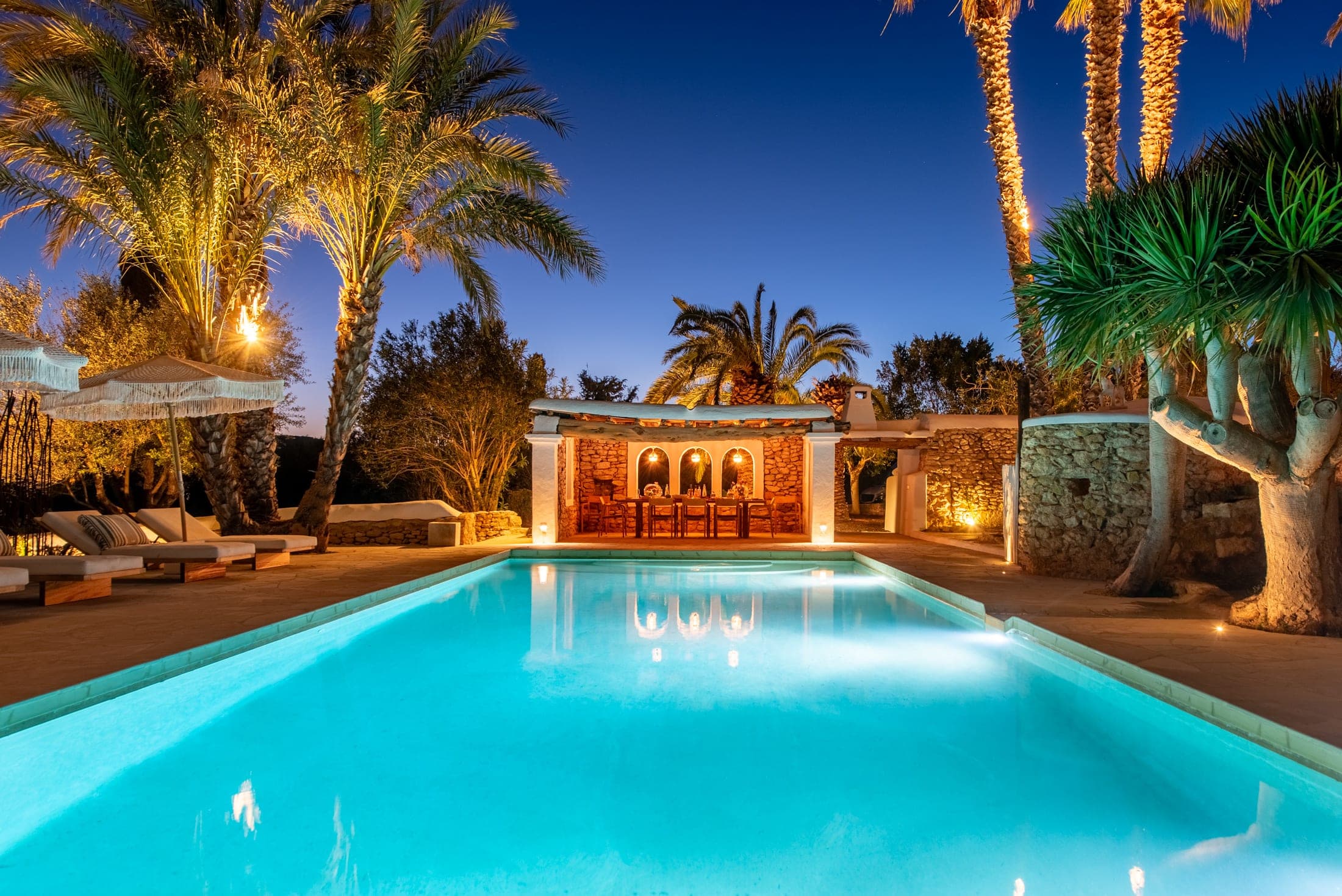 Finca in Ibiza with a lit pool under palm trees in the evening